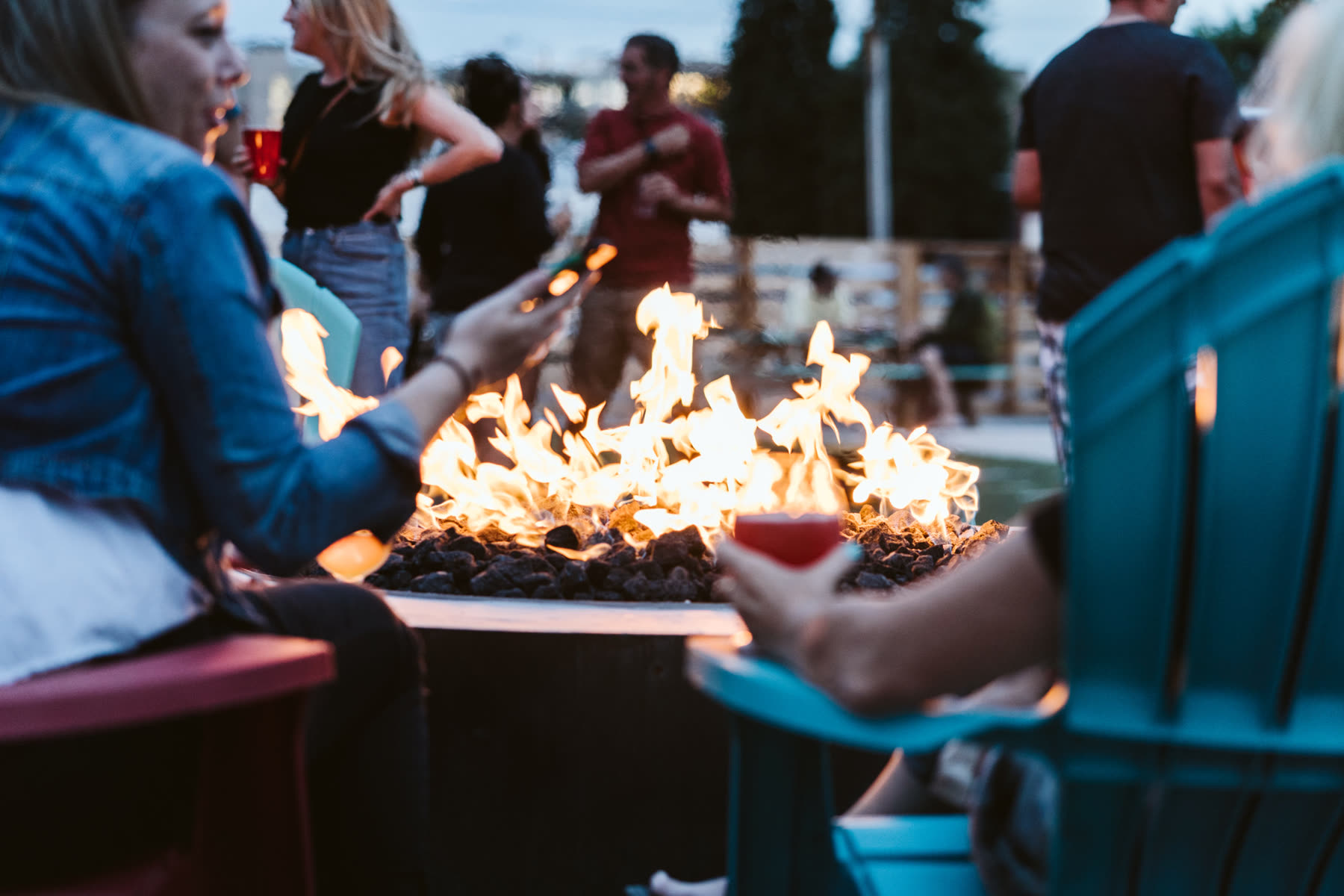 Friends around the fire pit at Backyard Tap, a glass of beer in hand