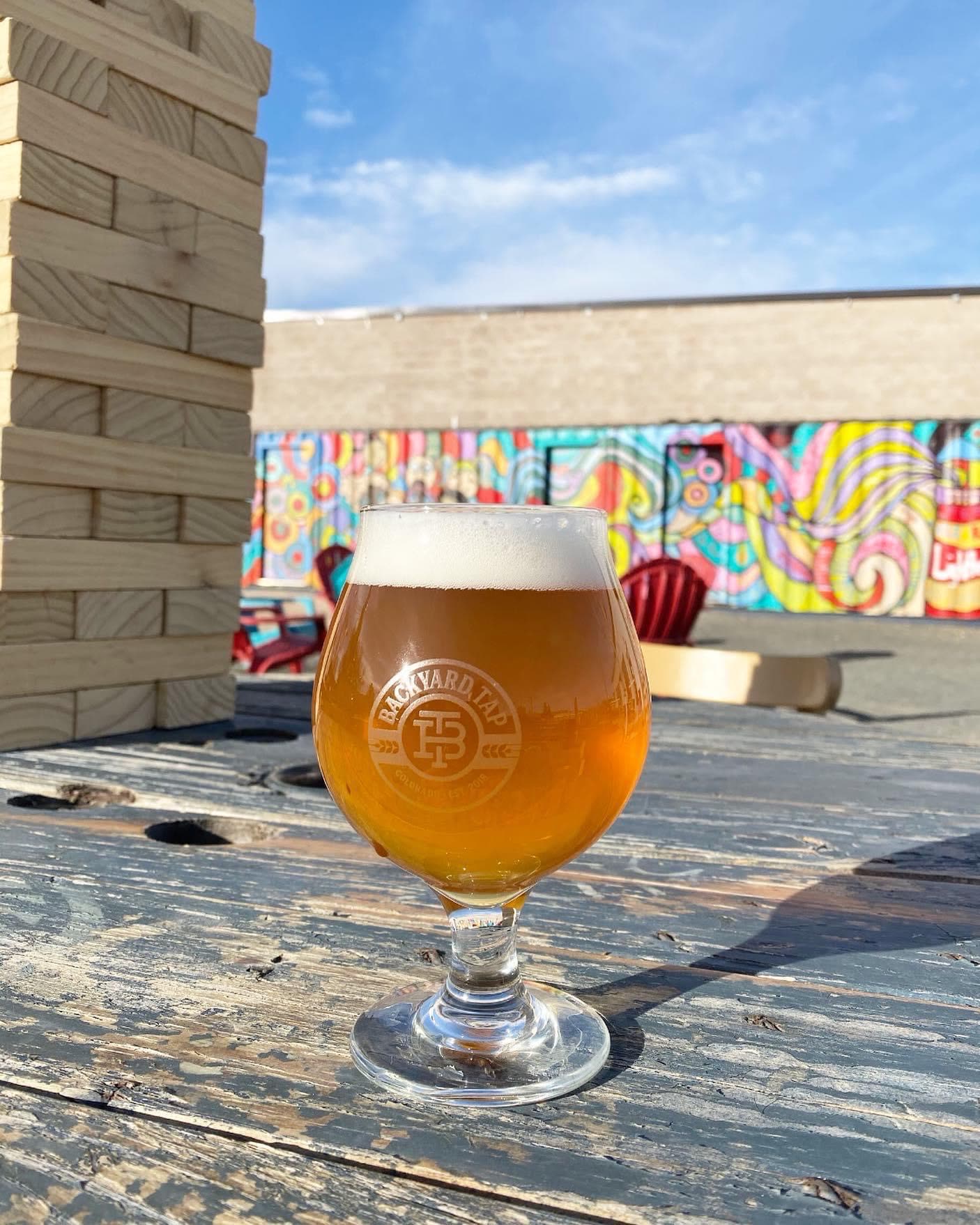 A Backyard Tap glass of beer on a picnic table in front of the yard's mural